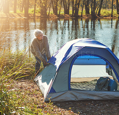 Buy stock photo Shot of a senior woman setting up a tent while camping in the wilderness