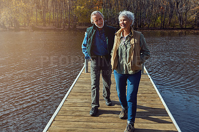 Buy stock photo Shot of a senior couple going for a walk on a jetty next to a lake