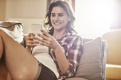 Buy stock photo Shot of a young woman relaxing on the sofa at home and using a mobile phone