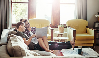 Buy stock photo Shot of a young couple using a laptop and going through paperwork together on the sofa at home