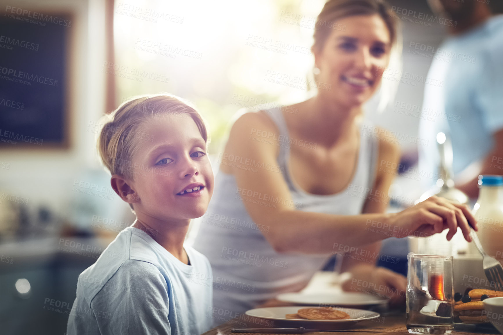 Buy stock photo Cropped shot of a little boy having breakfast with his mom sitting in the background