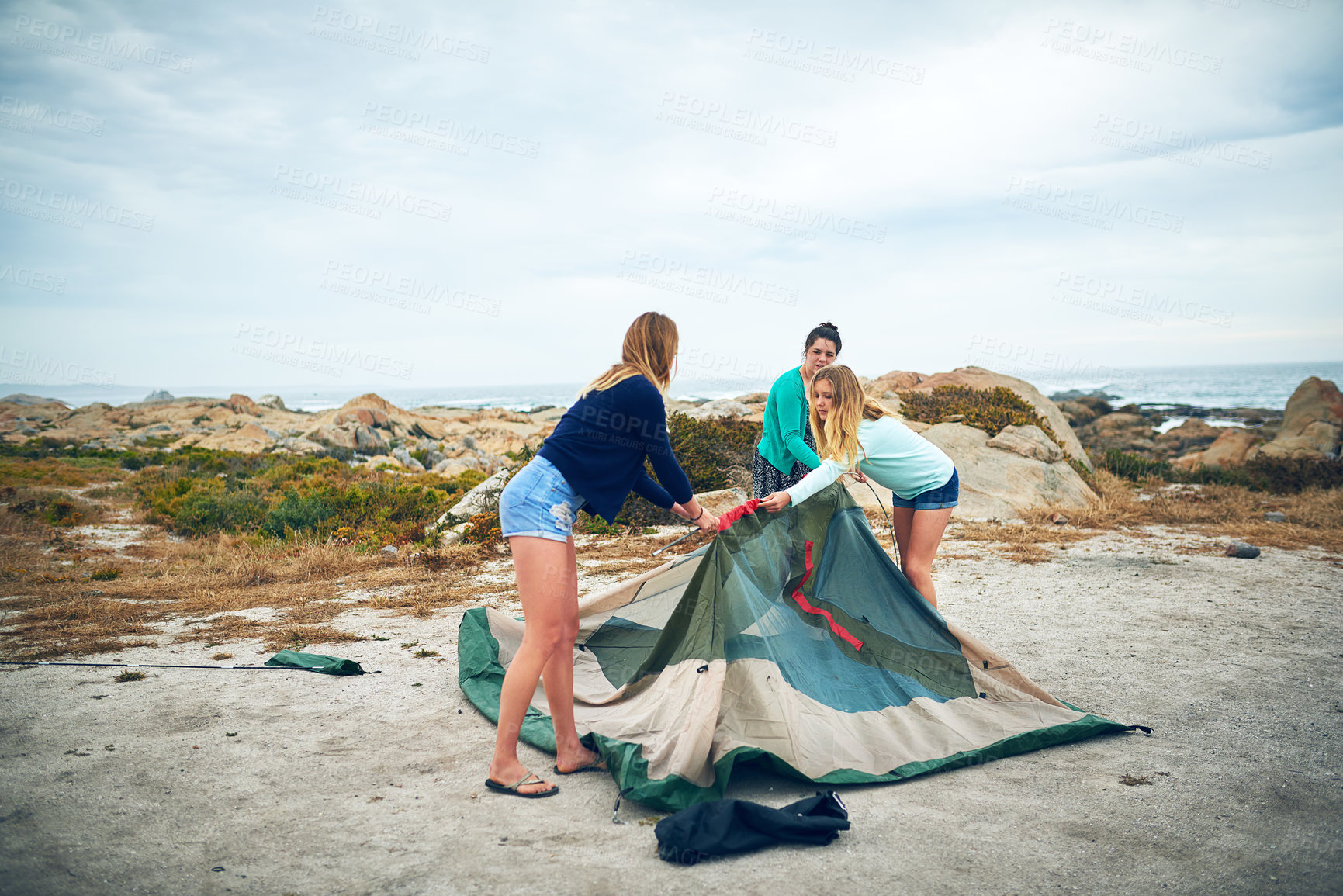 Buy stock photo Women, tent setup and camping at beach for vacation trip, outdoor and together for bonding. Girl, travel and adventure in nature for shelter, friends activity or campsite under cloudy sky for holiday