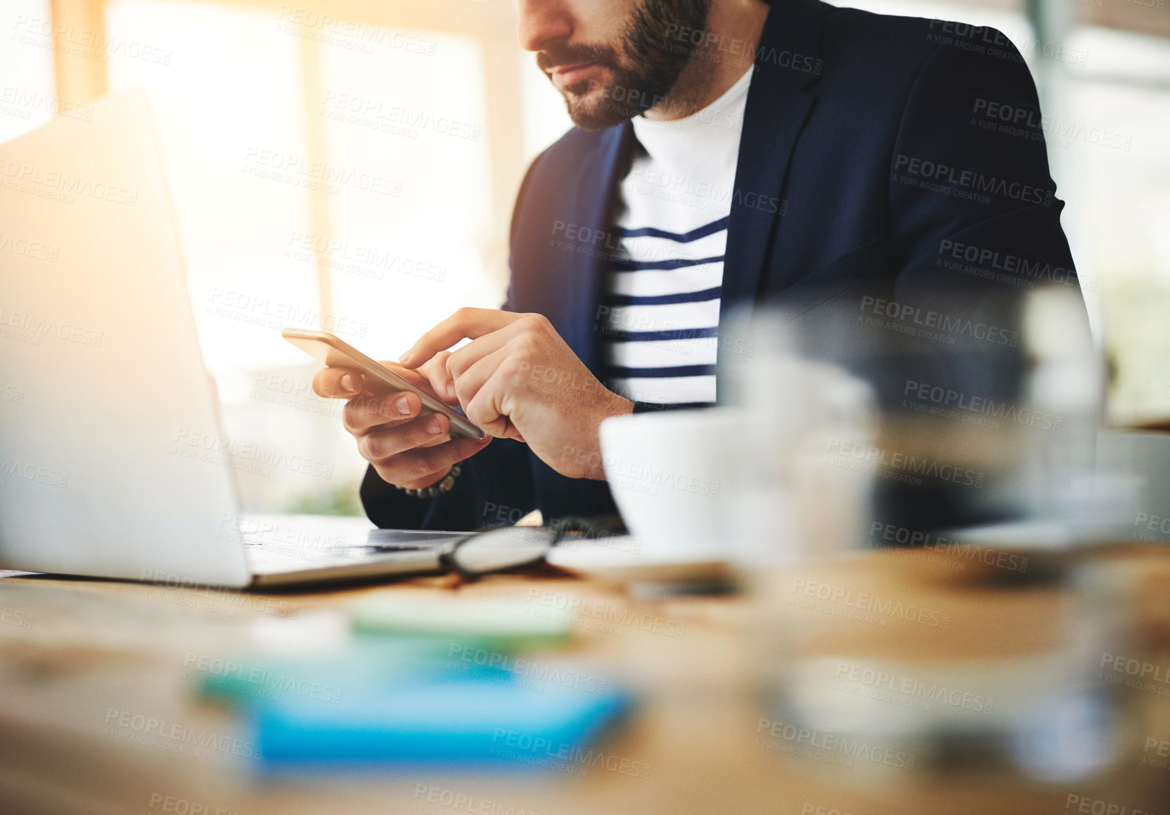 Buy stock photo Cropped shot of a young businessman using a mobile phone and laptop at his work desk