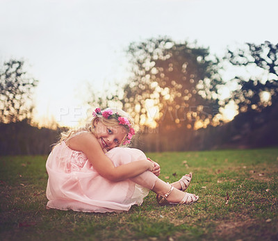 Buy stock photo Shot of a happy little girl sitting on the ground and looking at the camera outside in nature