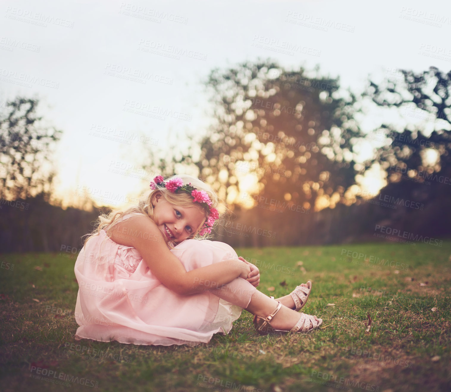 Buy stock photo Shot of a happy little girl sitting on the ground and looking at the camera outside in nature