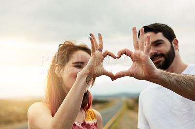 Buy stock photo Shot of two young friends putting their hands together to make a heart shape  while standing outside next to a road