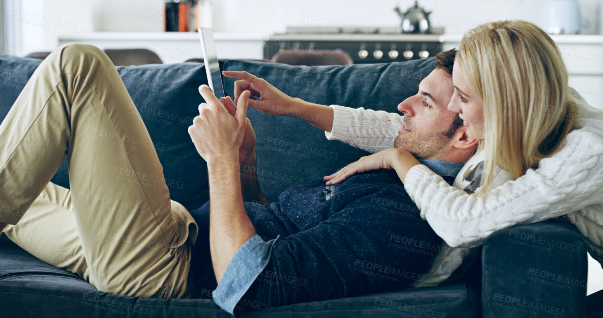 Buy stock photo Cropped shot of an affectionate young couple using a digital tablet while lying on their sofa at home