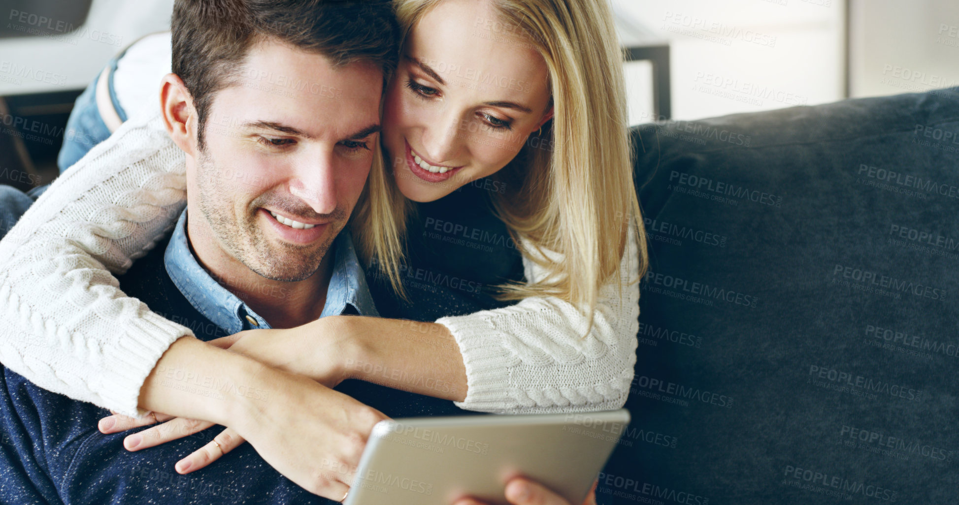 Buy stock photo Cropped shot of an affectionate young couple using a digital tablet while sitting on their sofa at home