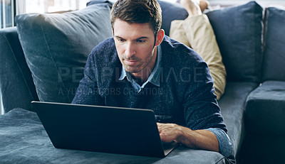 Buy stock photo Cropped shot of a handsome young man using his laptop while relaxing on the sofa at home