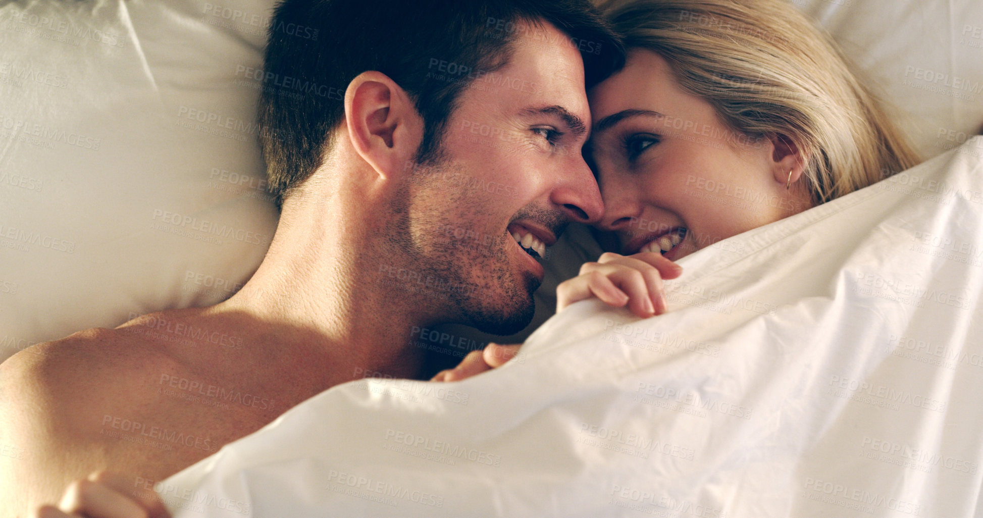 Buy stock photo High angle shot of an affectionate young couple lying in bed together
