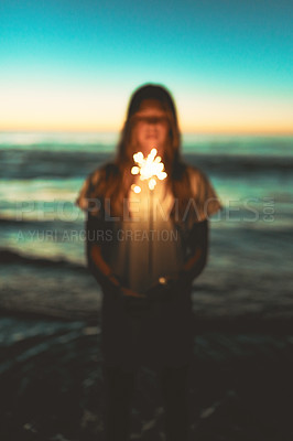 Buy stock photo Shot of a young woman holding a sparkler at the beach at night