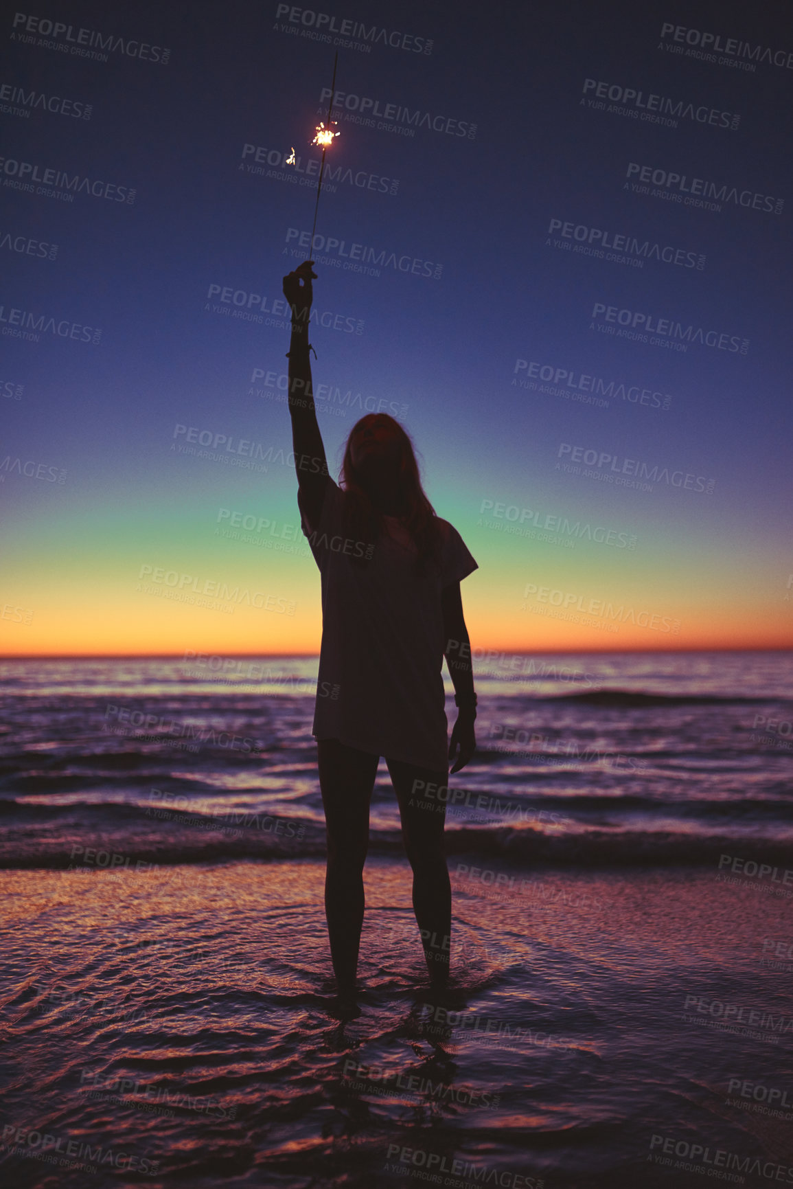 Buy stock photo Shot of a young woman holding a sparkler at the beach at night