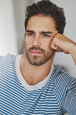 Buy stock photo Shot of a young man sitting at home deep in thought