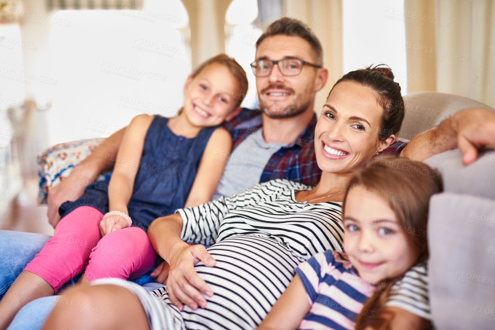 Buy stock photo Portrait of a happy young family posing on their sofa at home