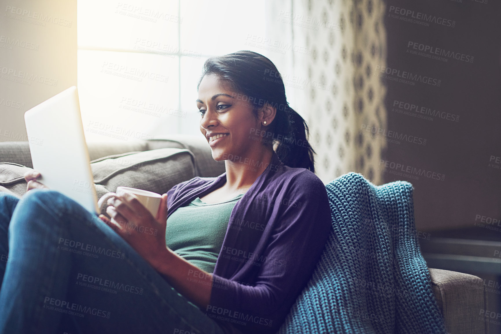 Buy stock photo Home, Indian woman and tablet on couch to laugh, relax and comfortable with technology in living room. Apartment, happy girl or digital for streaming comedy, funny film or watch movie with coffee cup