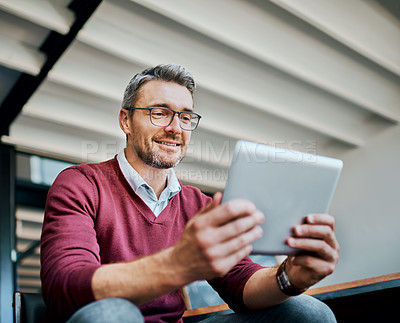 Buy stock photo Shot of a cheerful mature businessman working on his tablet while being seated in the office