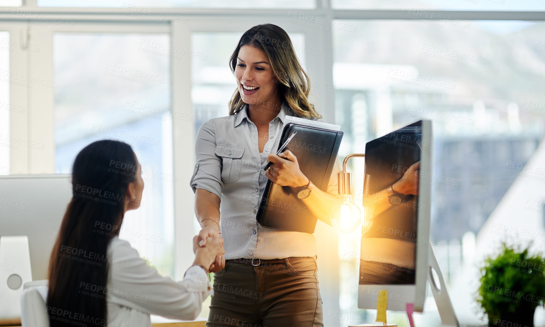Buy stock photo Shot of two young business women greeting each other with a handshake in the office at work