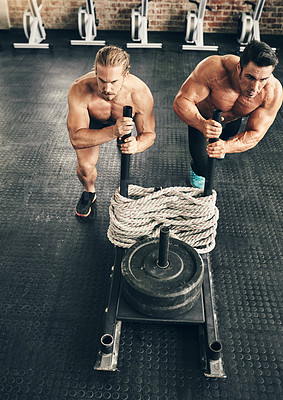 Buy stock photo Shot of two fit and determined young men making use of weights to workout in a gym together