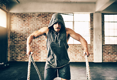 Buy stock photo Shot of a hooded and determined young man making use of ropes to workout in the gym