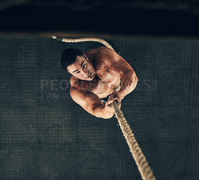Buy stock photo High angle shot of a fit and determined young man climbing a rope for strength exercise in a gym