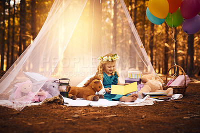 Buy stock photo Shot of a happy little girl reading a storybook while sitting on a blanket outside in the woods