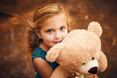 Buy stock photo Shot of a happy little girl looking at the camera and holding her teddy bear while standing outside in the woods