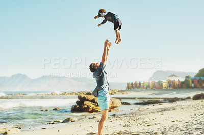 Buy stock photo Shot of a young Father tossing his son into the air at the beach