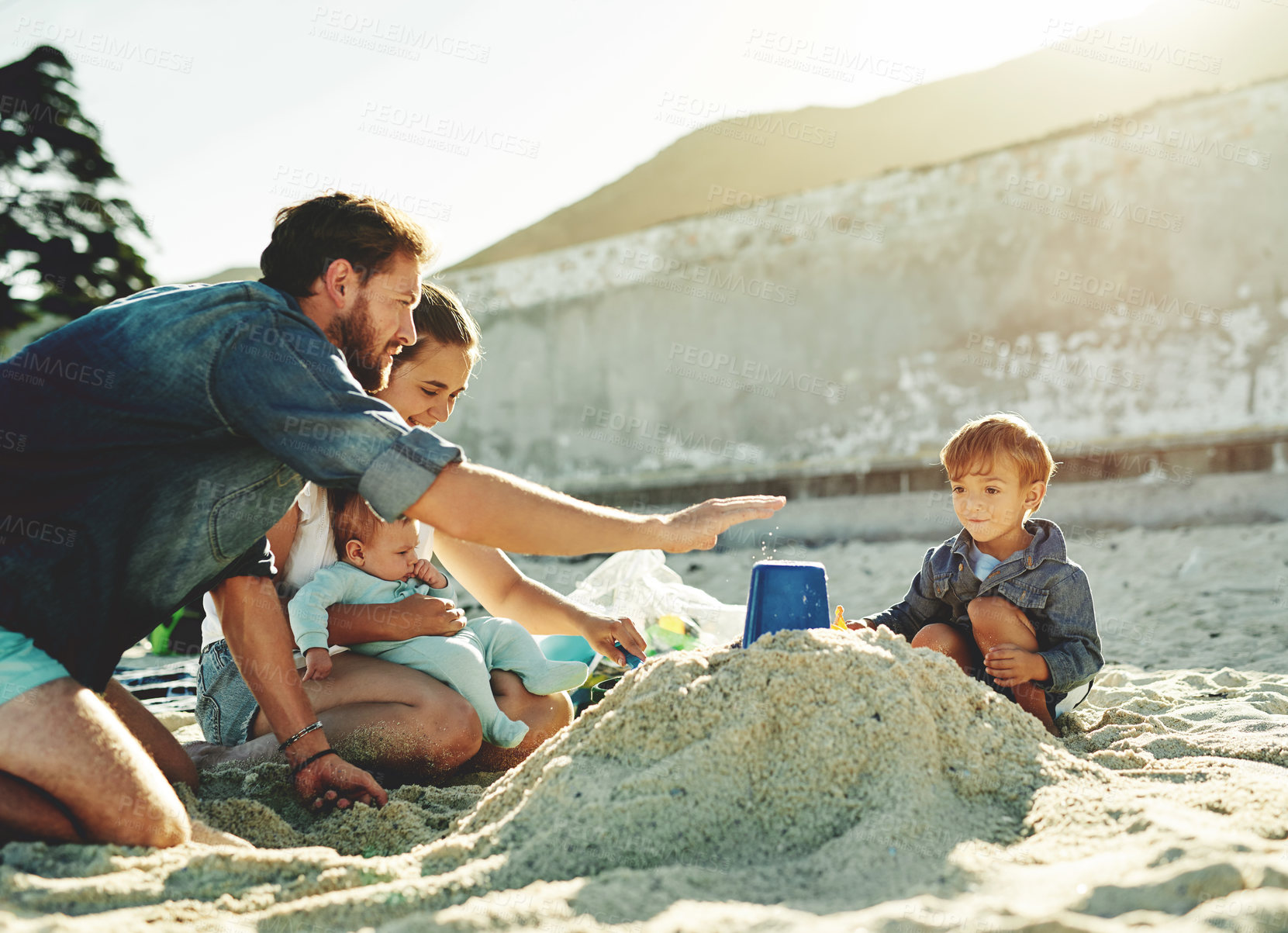 Buy stock photo Sandcastle help, parents and children at the beach with bonding, love and support. Baby, mom and dad together with kids playing in the sun with happiness and smile by the ocean and sea with family