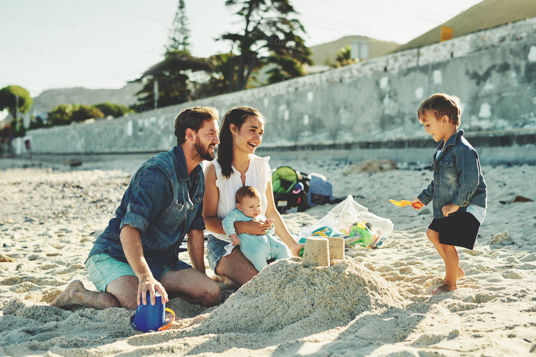 Buy stock photo Family, beach and fun with mother, dad and children together with sandcastle and vacation. Outdoor, happy people and summer holiday with sea and travel with love, care and support with baby by ocean 