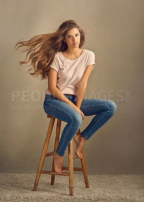 Buy stock photo Studio shot of a beautiful young woman sitting on a stool against a plain background