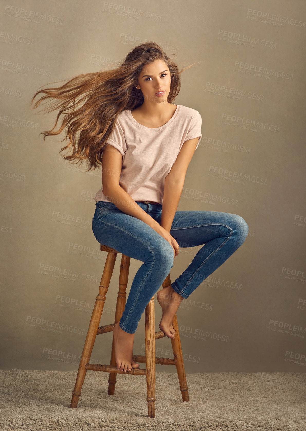 Buy stock photo Studio shot of a beautiful young woman sitting on a stool against a plain background