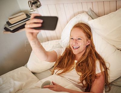 Buy stock photo Shot of a young woman taking a selfie laying in bed in the bedroom at home