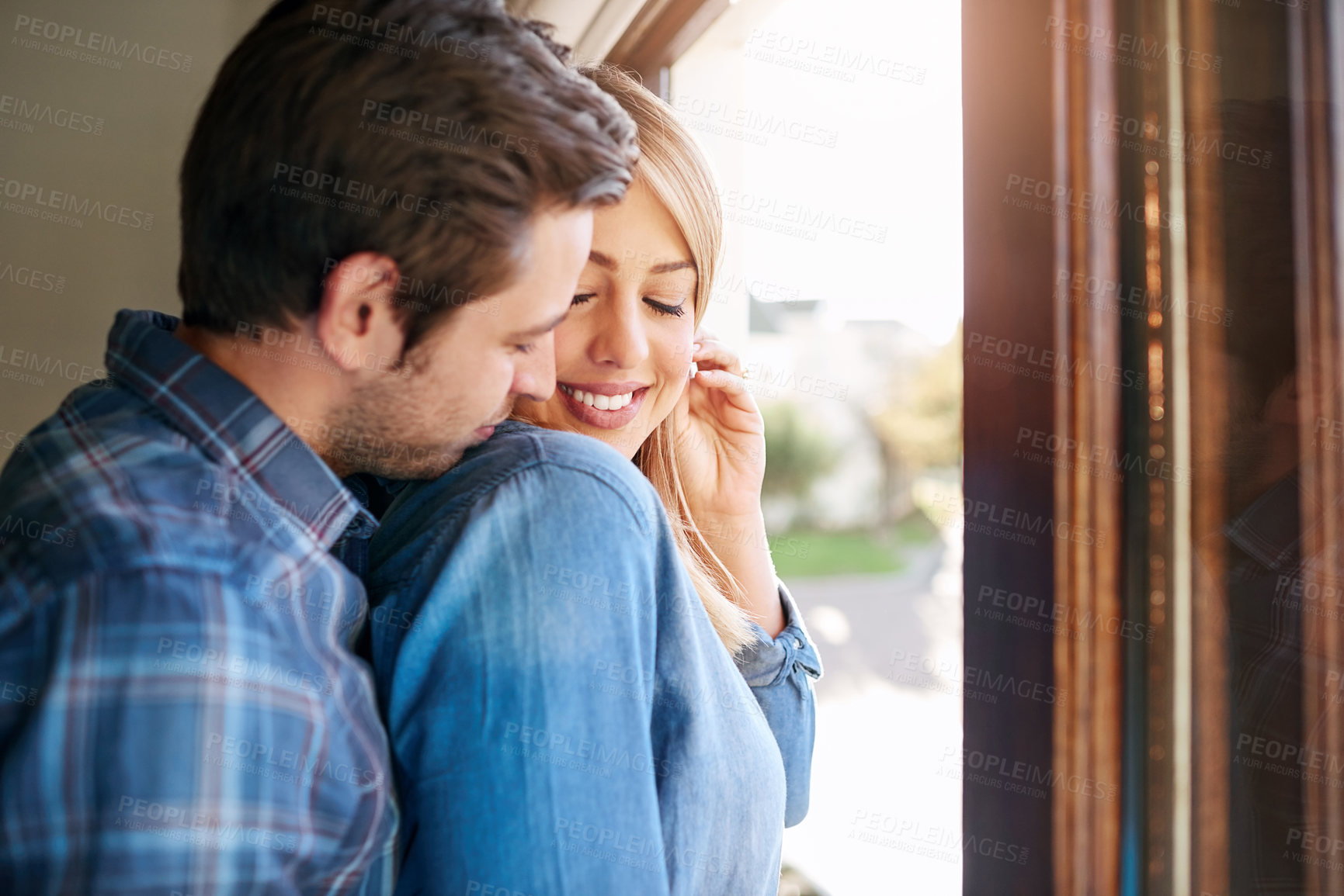 Buy stock photo Cropped shot of an affectionate young couple standing at a window in their home