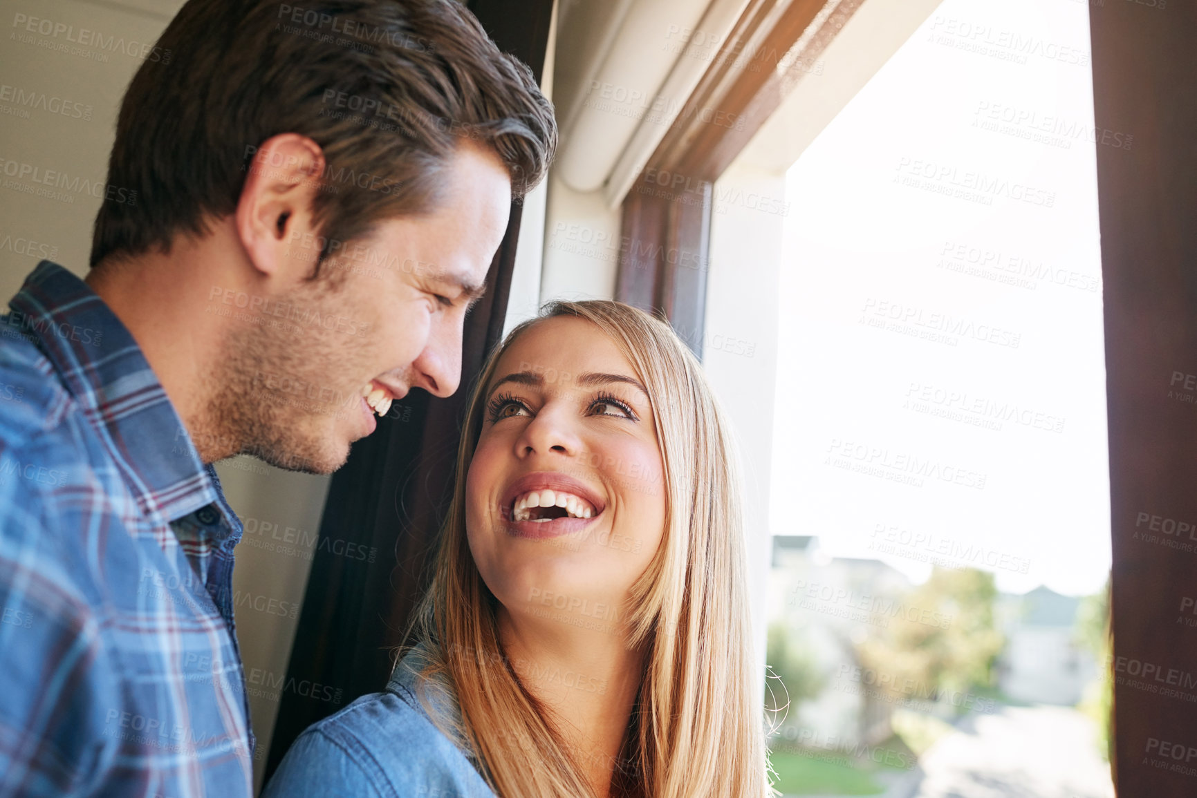 Buy stock photo Cropped shot of an affectionate young couple standing at a window in their home