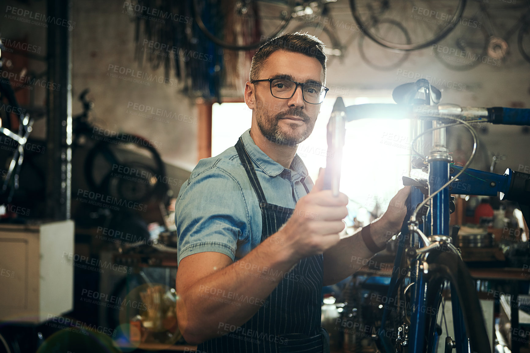 Buy stock photo Man, portrait or mechanic with bicycle in small business for repair, fix or maintenance. Young male person, cycle technician or bike engineer working on cycling vehcile, gears or hardware at workshop