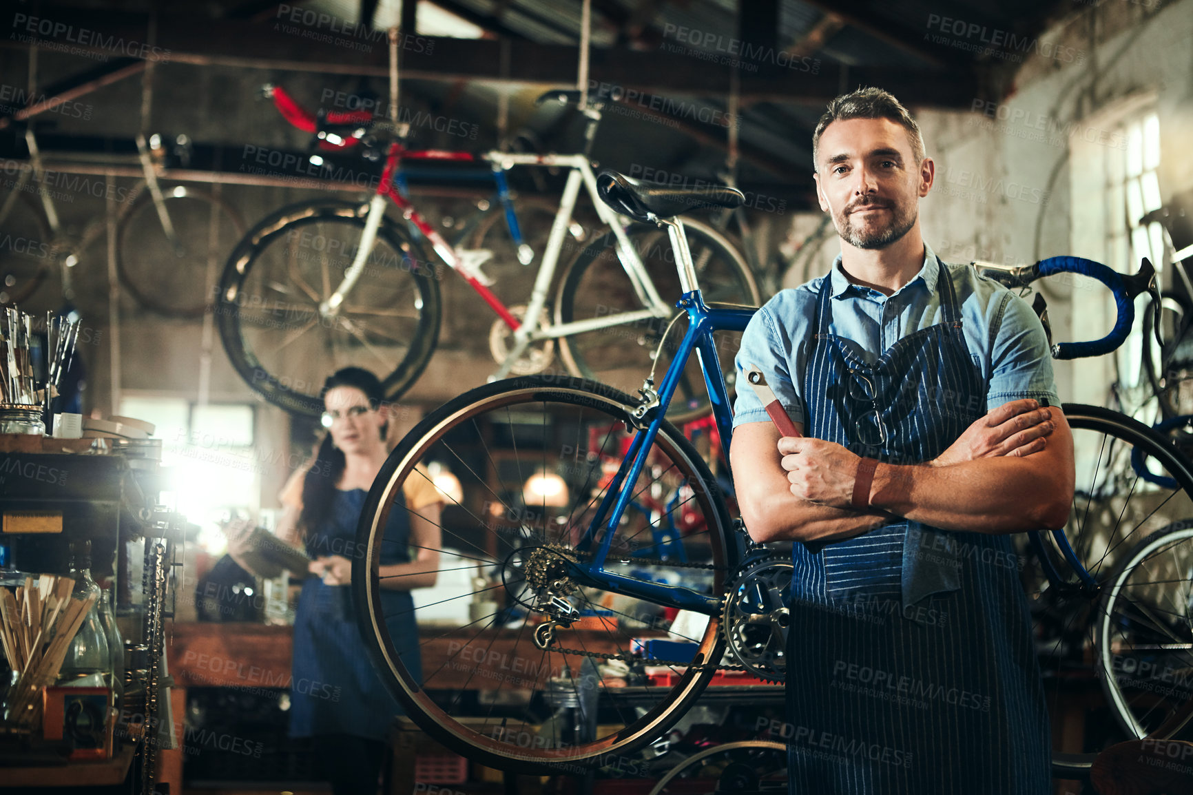 Buy stock photo Portrait of a mature man working in a bicycle repair shop with his coworker in the background