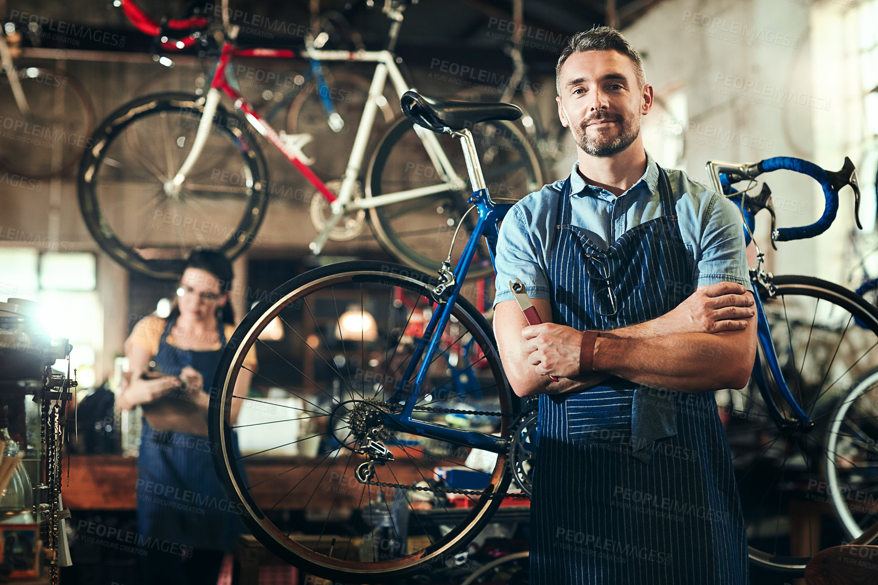 Buy stock photo Portrait of a mature man working in a bicycle repair shop with his coworker in the background