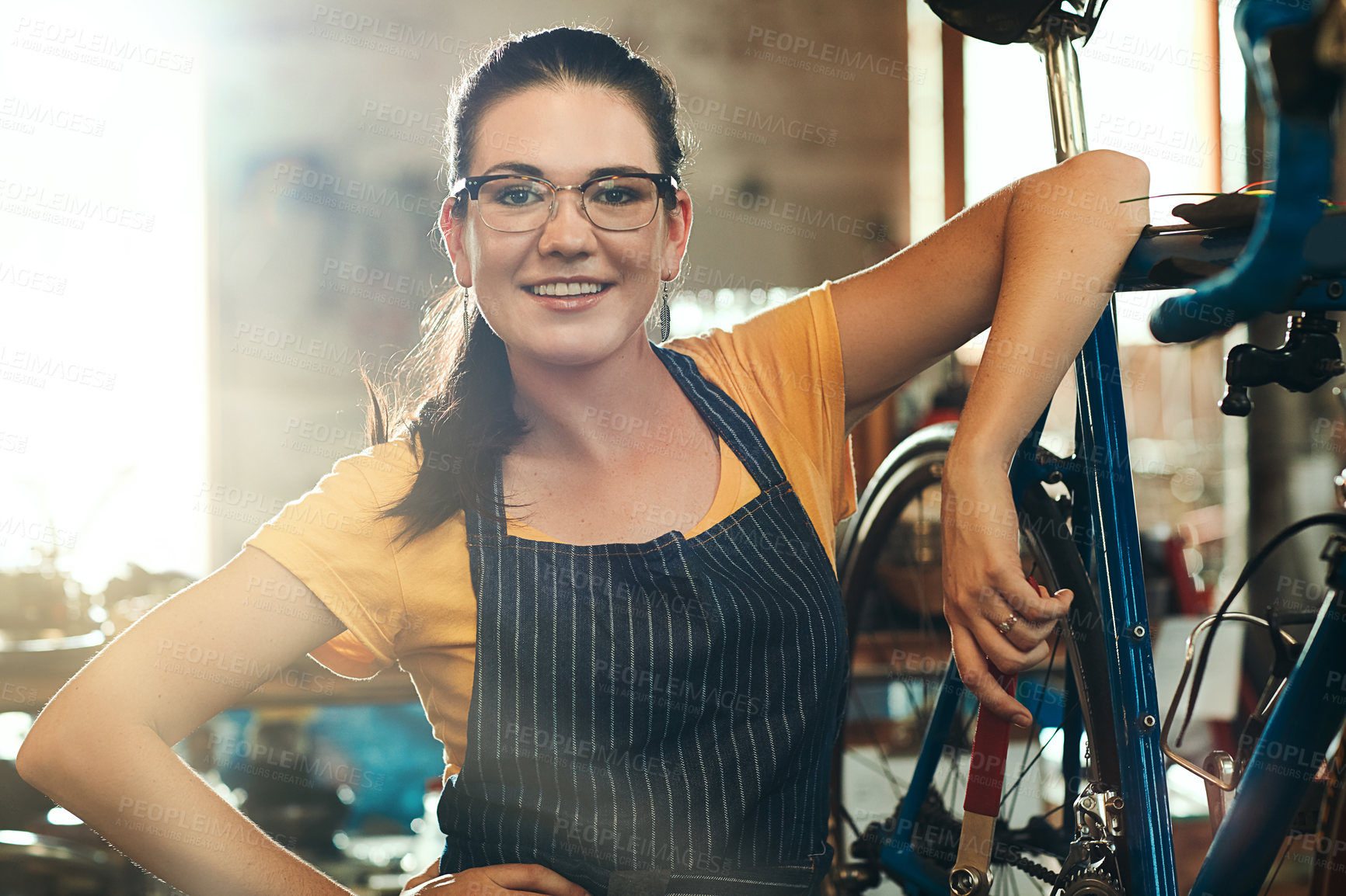 Buy stock photo Portrait of a young woman working in a bicycle repair shop