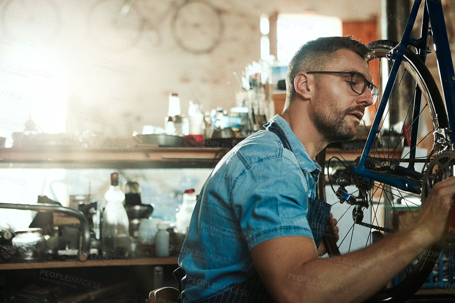 Buy stock photo Man, garage and serious as bicycle mechanic with equipment in startup and small business. Workshop, expert and tools as handyman with fixing bike at repair or maintenance shop and diy service