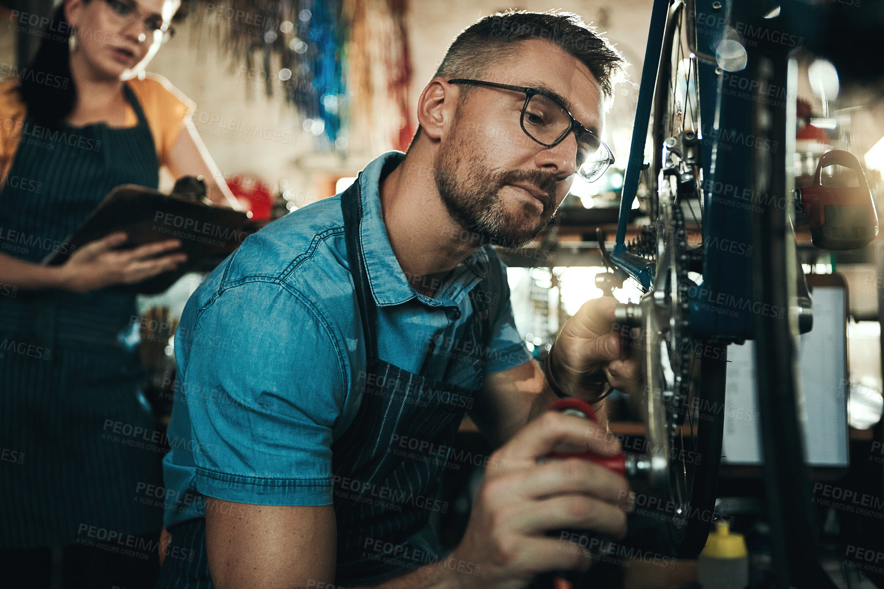 Buy stock photo Fixing bicycle, mechanic and man with woman for startup, garage tools and clipboard for service checklist. Mentor guy, bike inspection and girl with notes for technician internship in repair workshop