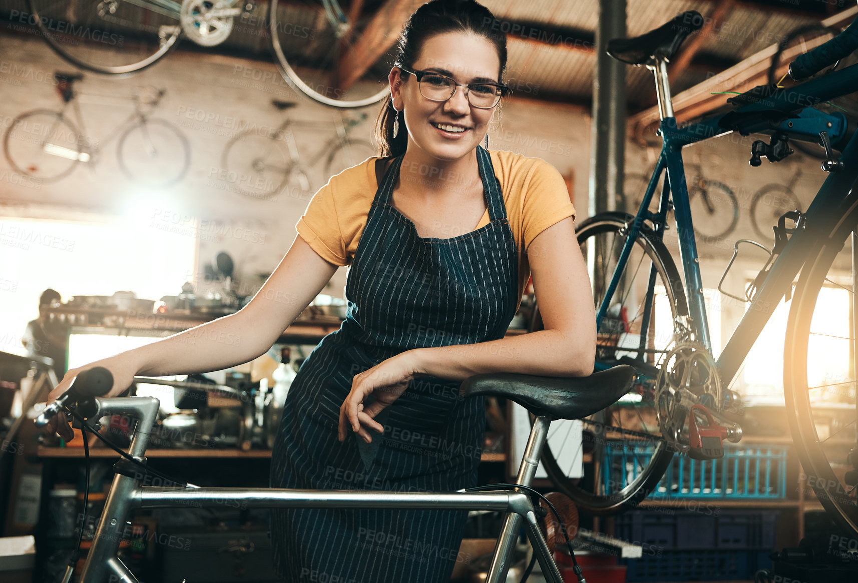 Buy stock photo Woman, bicycle shop and portrait for maintenance job, startup with transport service. Bike, mechanic and female entrepreneur in workshop with glasses, happiness for sustainable business with apron