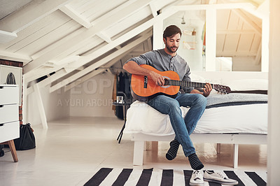 Buy stock photo Shot of a handsome young man practising guitar at home