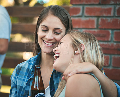 Buy stock photo Shot of two happy young women enjoying some beers at a get together with their friends