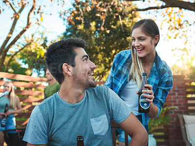 Buy stock photo Shot of a young man and woman having beers and talking at a barbecue with friends