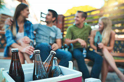 Buy stock photo Shot of bottled beers chilling in a cooler box with a group of friends hanging out in the background