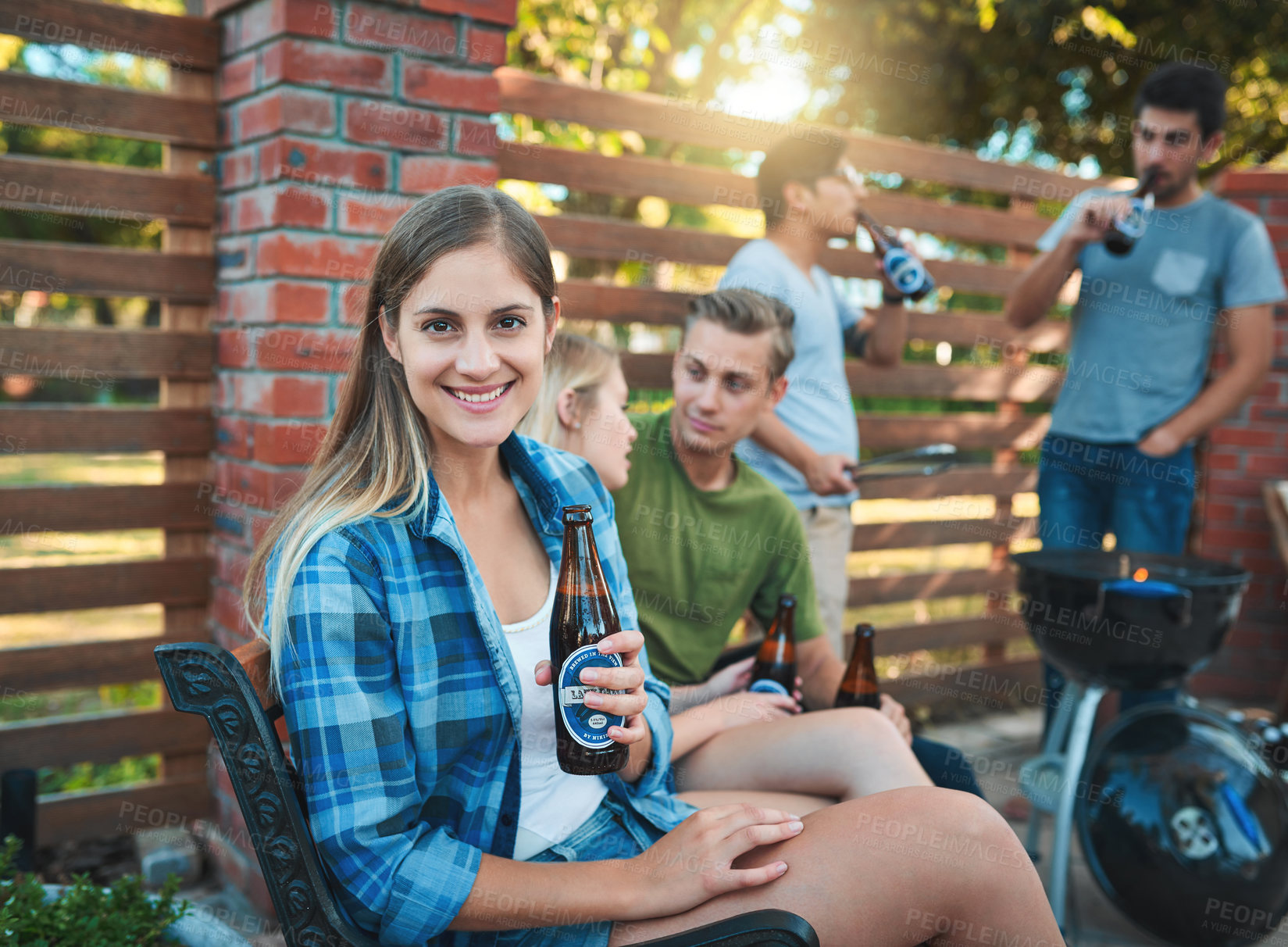 Buy stock photo Shot of a happy young woman enjoying a beer at a barbecue with her friends