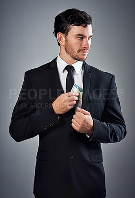 Buy stock photo Studio shot of a young businessman concealing money in his jacket against a gray background