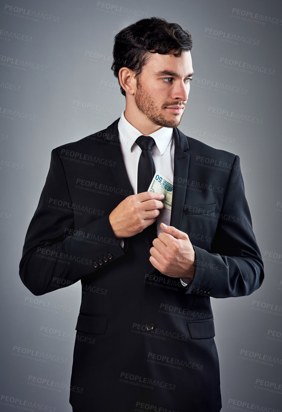 Buy stock photo Studio shot of a young businessman concealing money in his jacket against a gray background