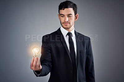 Buy stock photo Studio shot of a young businessman holding a glowing lightbulb against a gray background