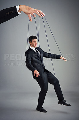 Buy stock photo Studio shot of a young businessman being controlled like a puppet by a giant hand against a gray background
